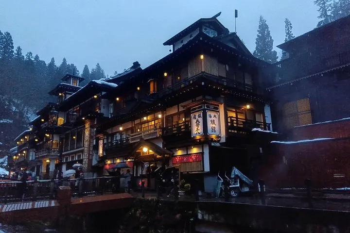 The wooden inns of Ginzan Onsen lit up at blue hour on a rainy evening, snow on the rooftops