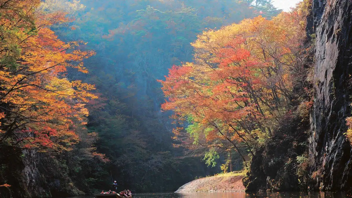 Red and orange autumn leaves on the cliffs of Geibikei Gorge above the still green river