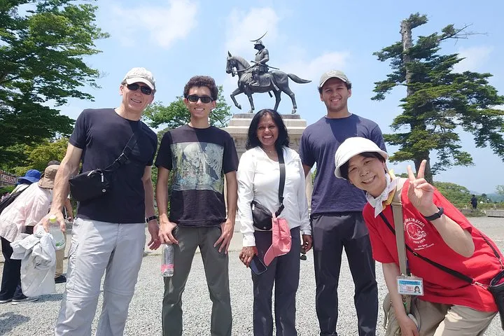 A small tour group posing with their guide below the bronze horseback statue of Date Masamune at Sendai Castle