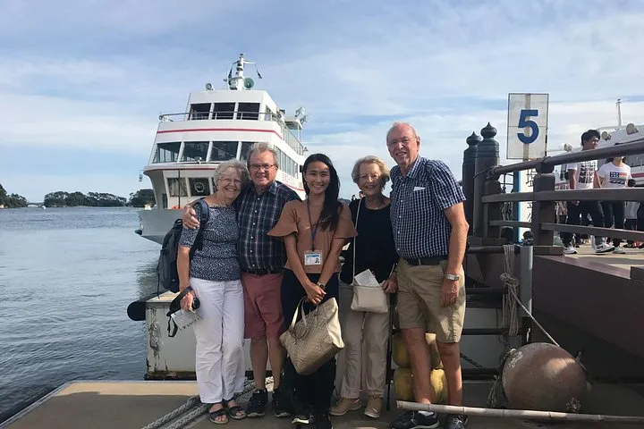 A group of travellers with their guide on the Matsushima pier in front of a white sightseeing boat