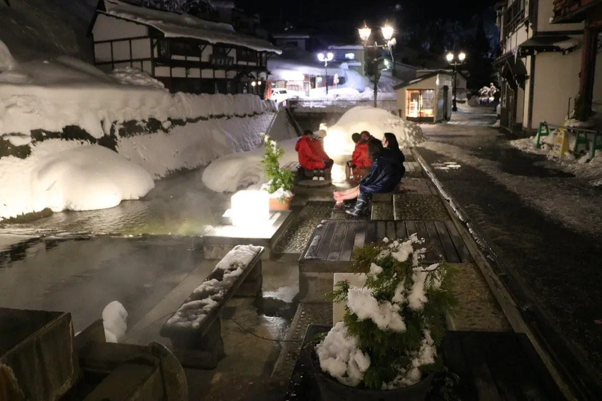 Snow banks and glowing lamps along the stream beside the footbath at night