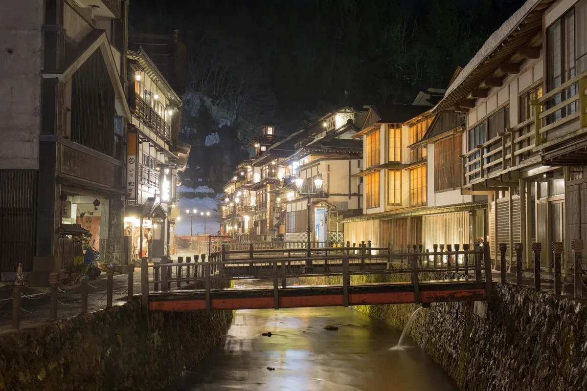 Lit wooden ryokan and a small bridge over the river at dusk