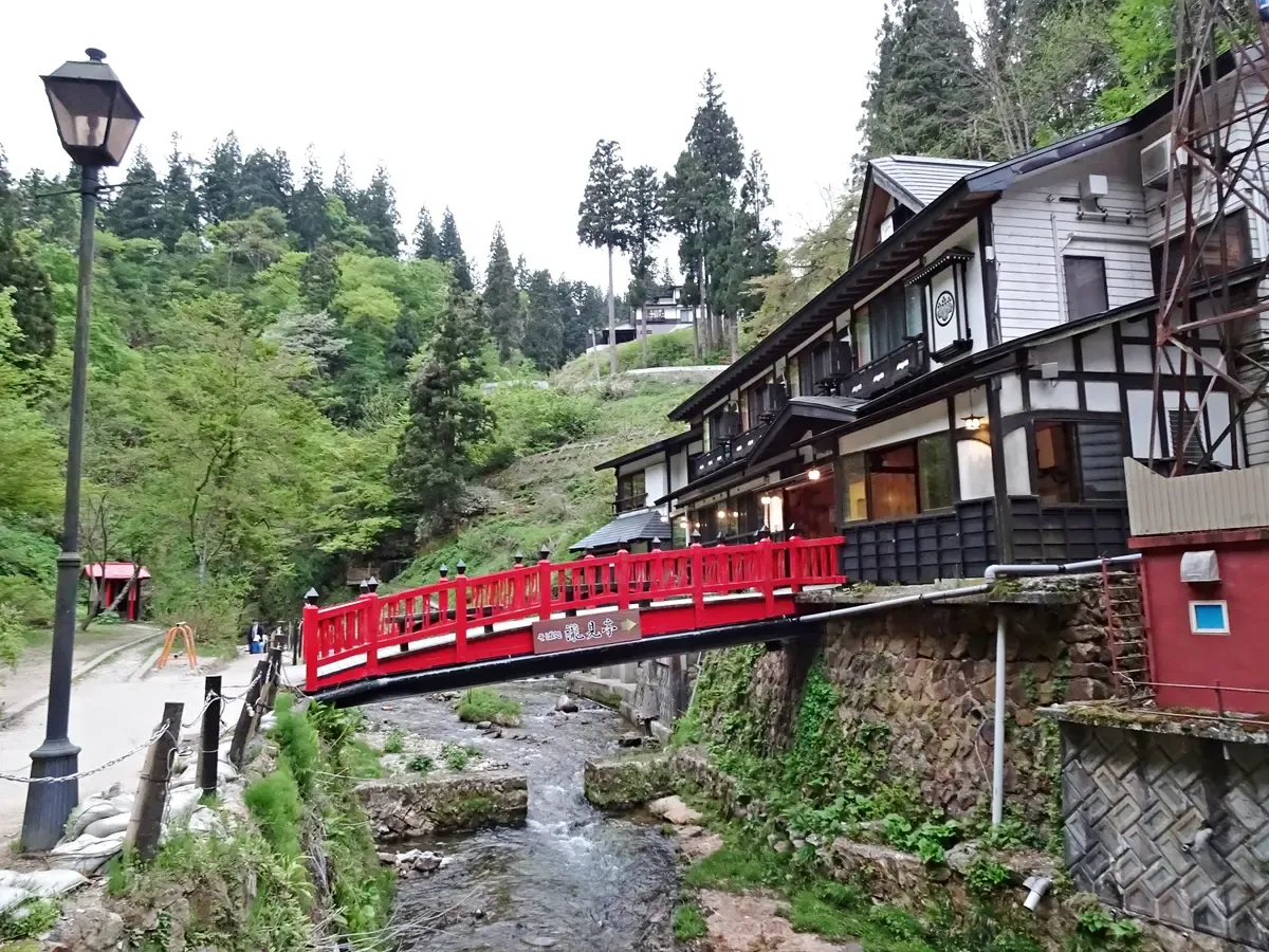 Red wooden footbridge over the stream beside a traditional inn in Ginzan Onsen on a green spring day
