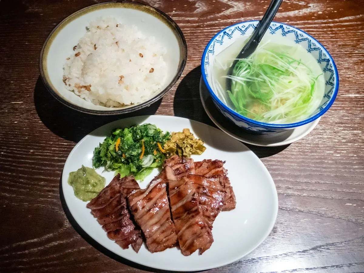 Grilled beef tongue set meal with barley rice and tail soup on a wooden table in Sendai