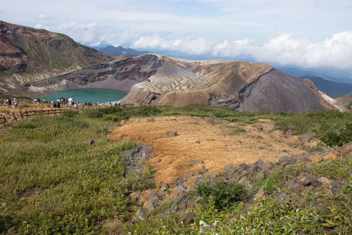 Green crater lake framed by volcanic slopes and grassland