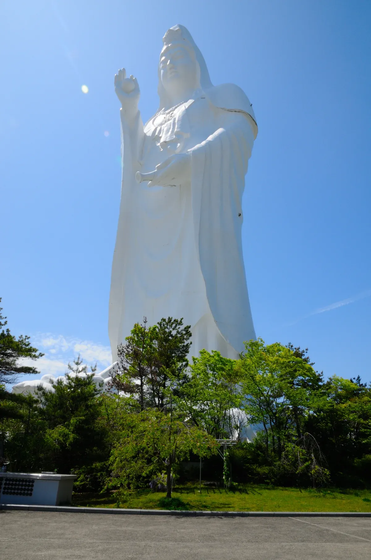 White Daikannon statue rising above trees under a clear sky