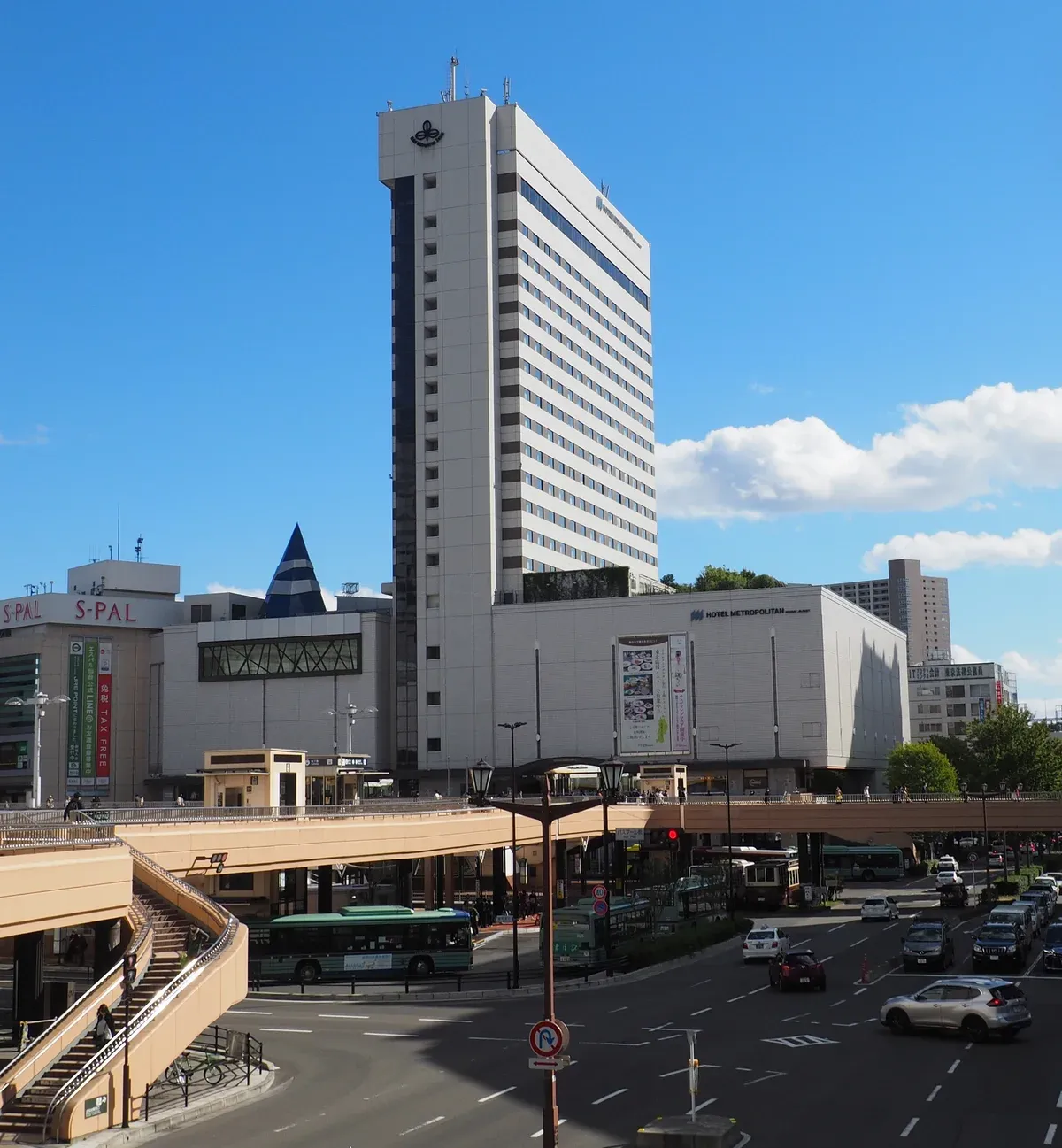Hotel Metropolitan Sendai tower rising beside the station's elevated walkway under a blue sky