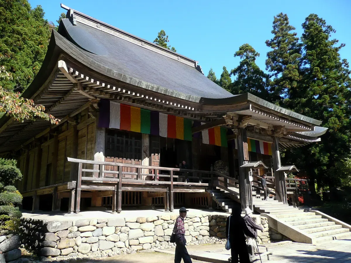 Wooden Konponchudo hall with a sweeping roof and stone base among tall cedars