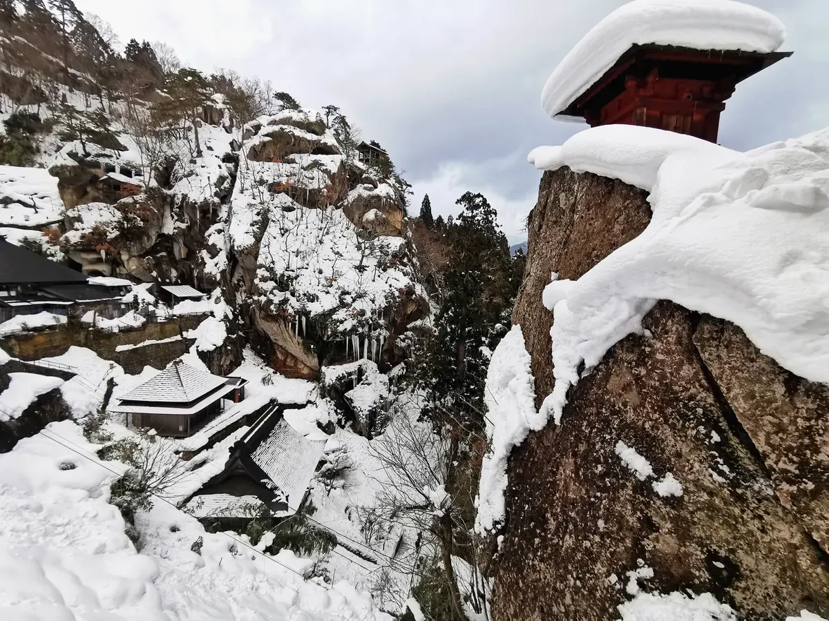 Snow piled on rock pinnacles and a small hall along the Yamadera path in winter