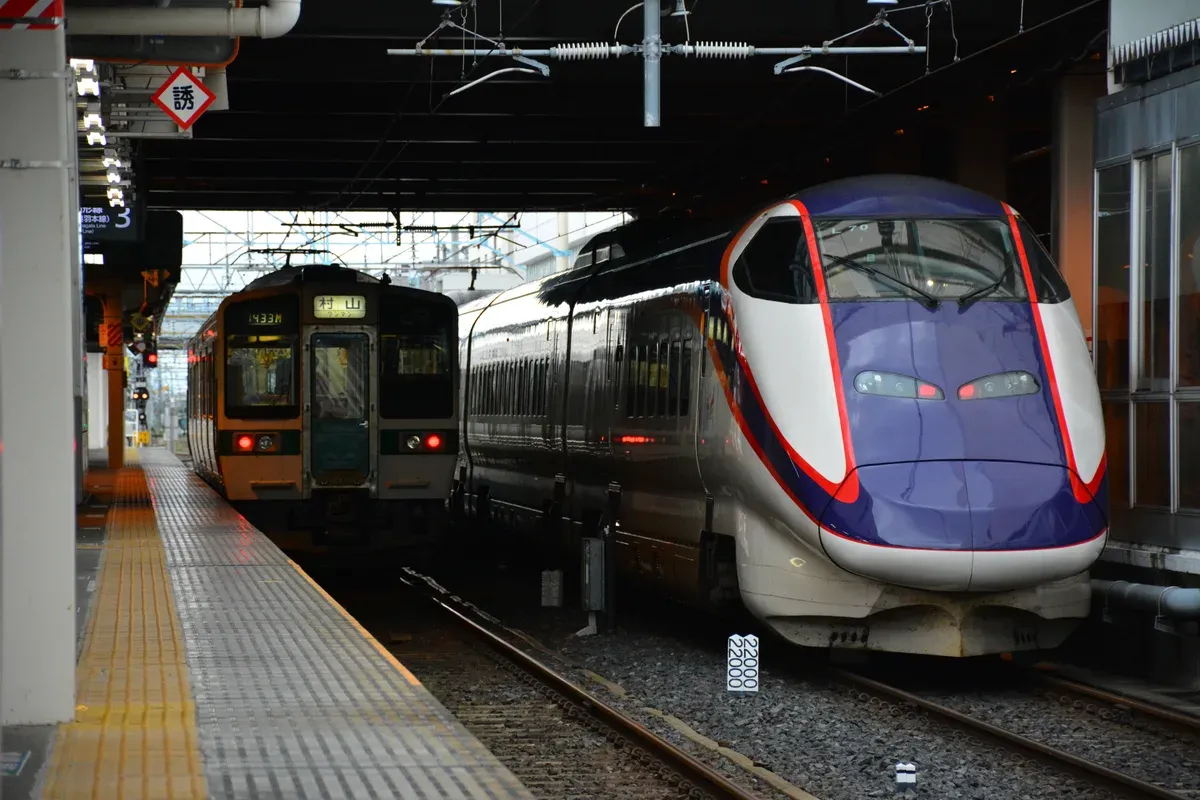 Purple and white Yamagata Shinkansen E3 train beside a local train at the platform of Yamagata Station